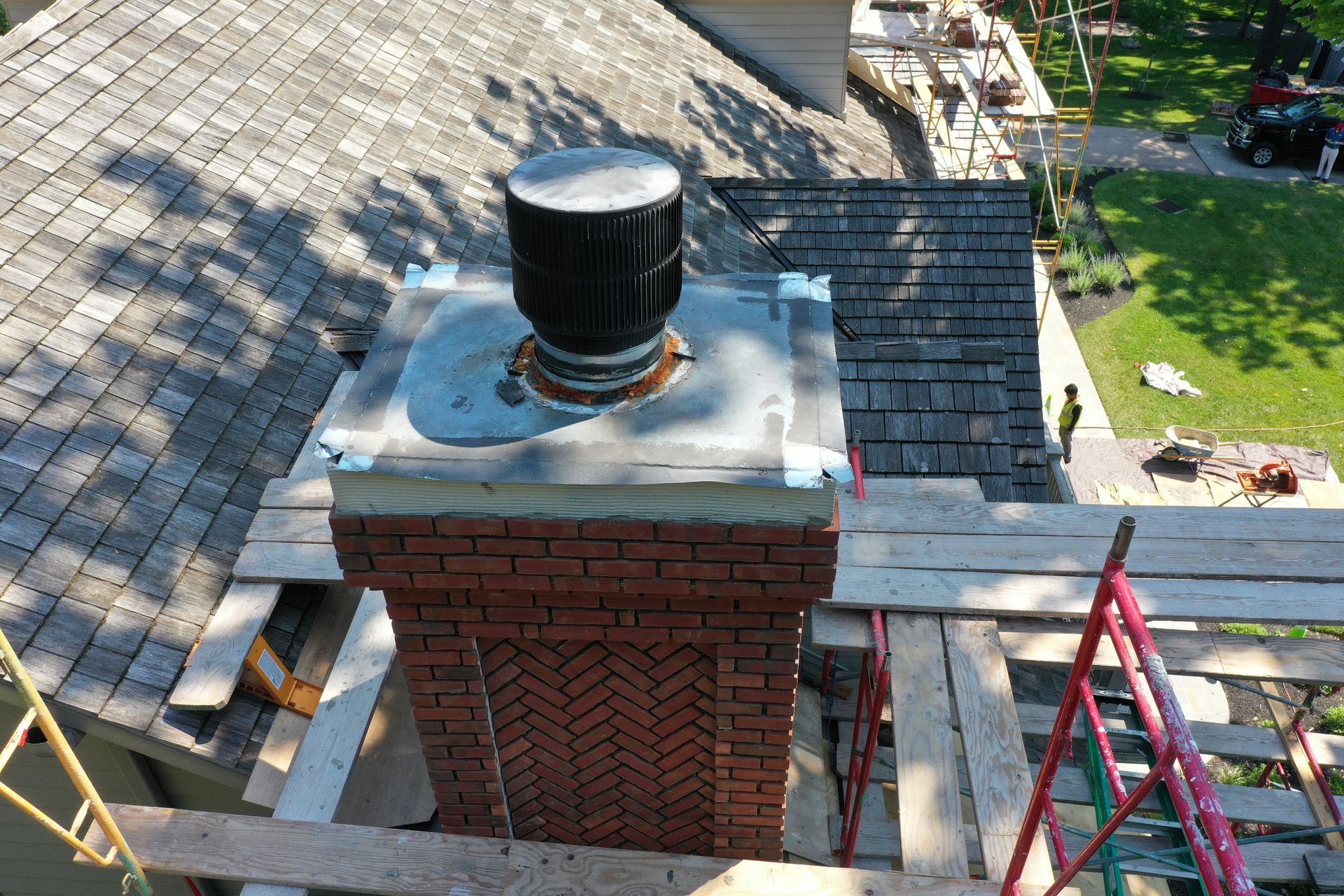 Chimney under repair with scaffolding on a shingled roof; red brick and gray metal components.