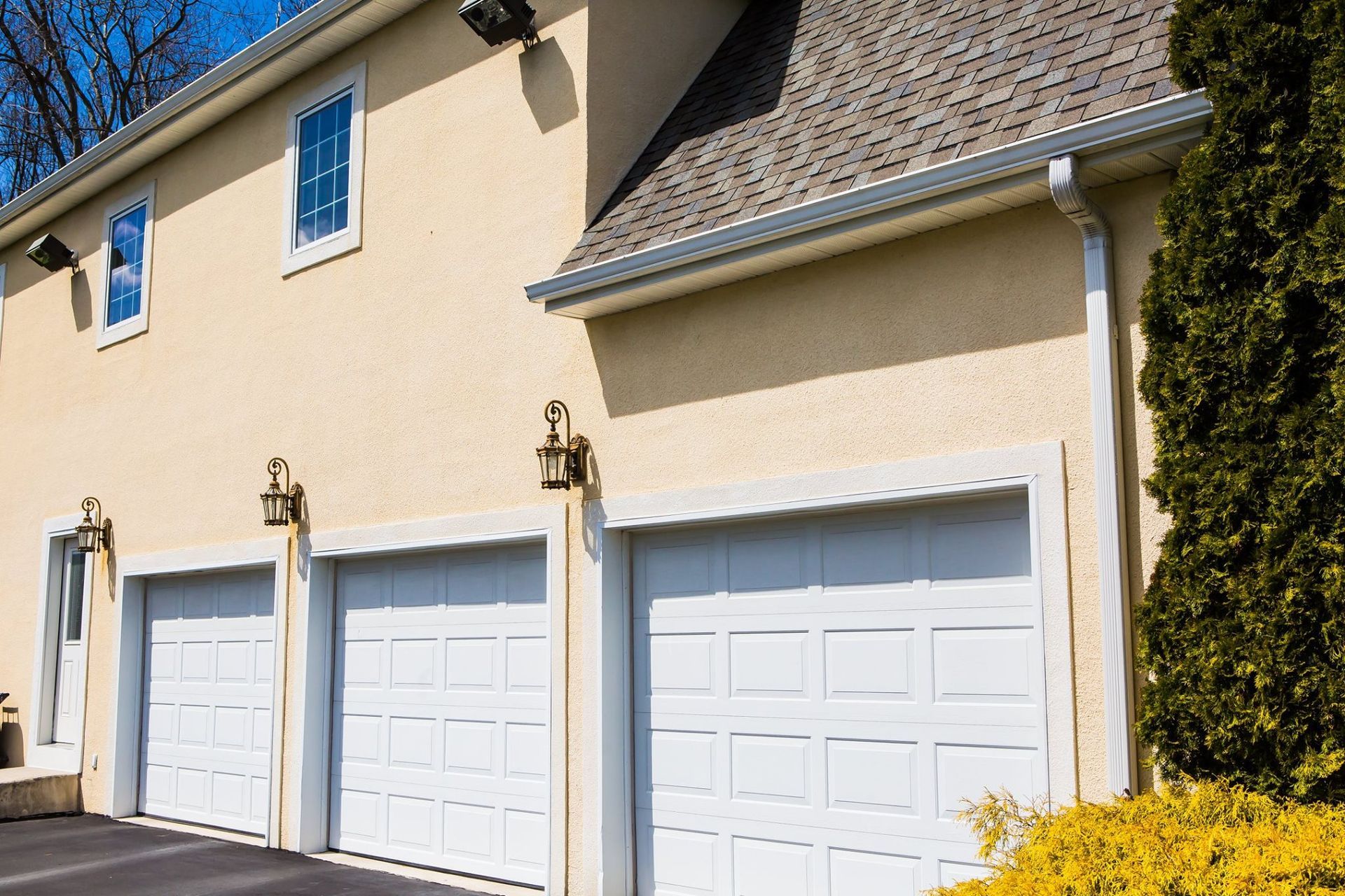 Three white garage doors on a beige stucco house with a gray roof and gutter system.
