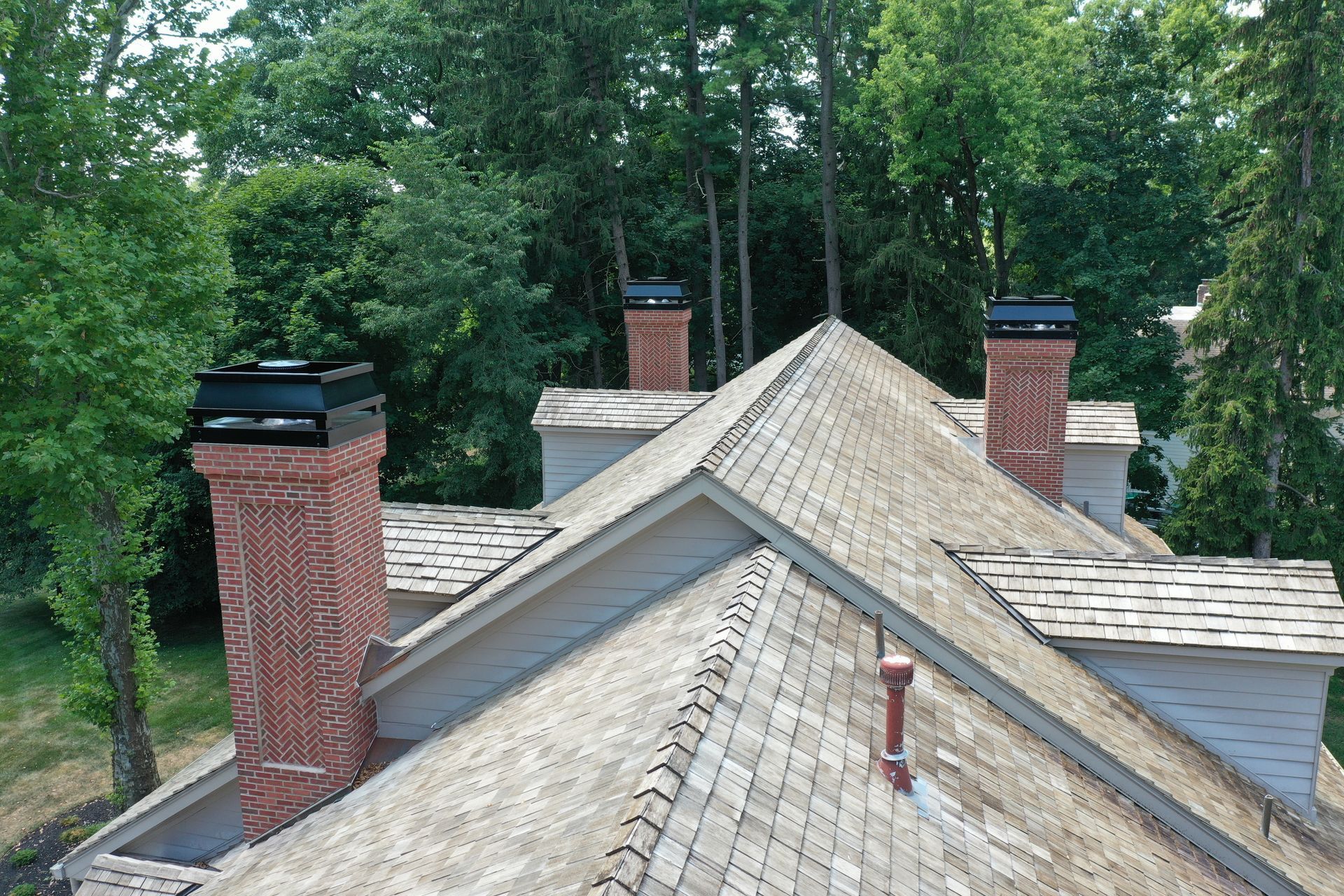 View of a house roof with three brick chimneys and black chimney caps.