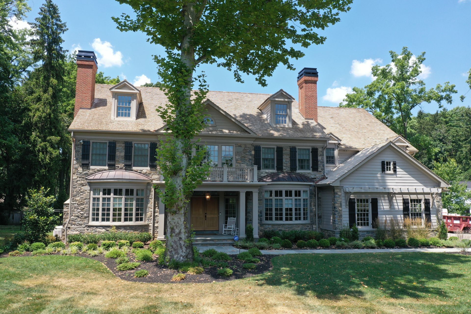 Stone house with a brown roof, black shutters, and two red brick chimneys, under a bright blue sky.