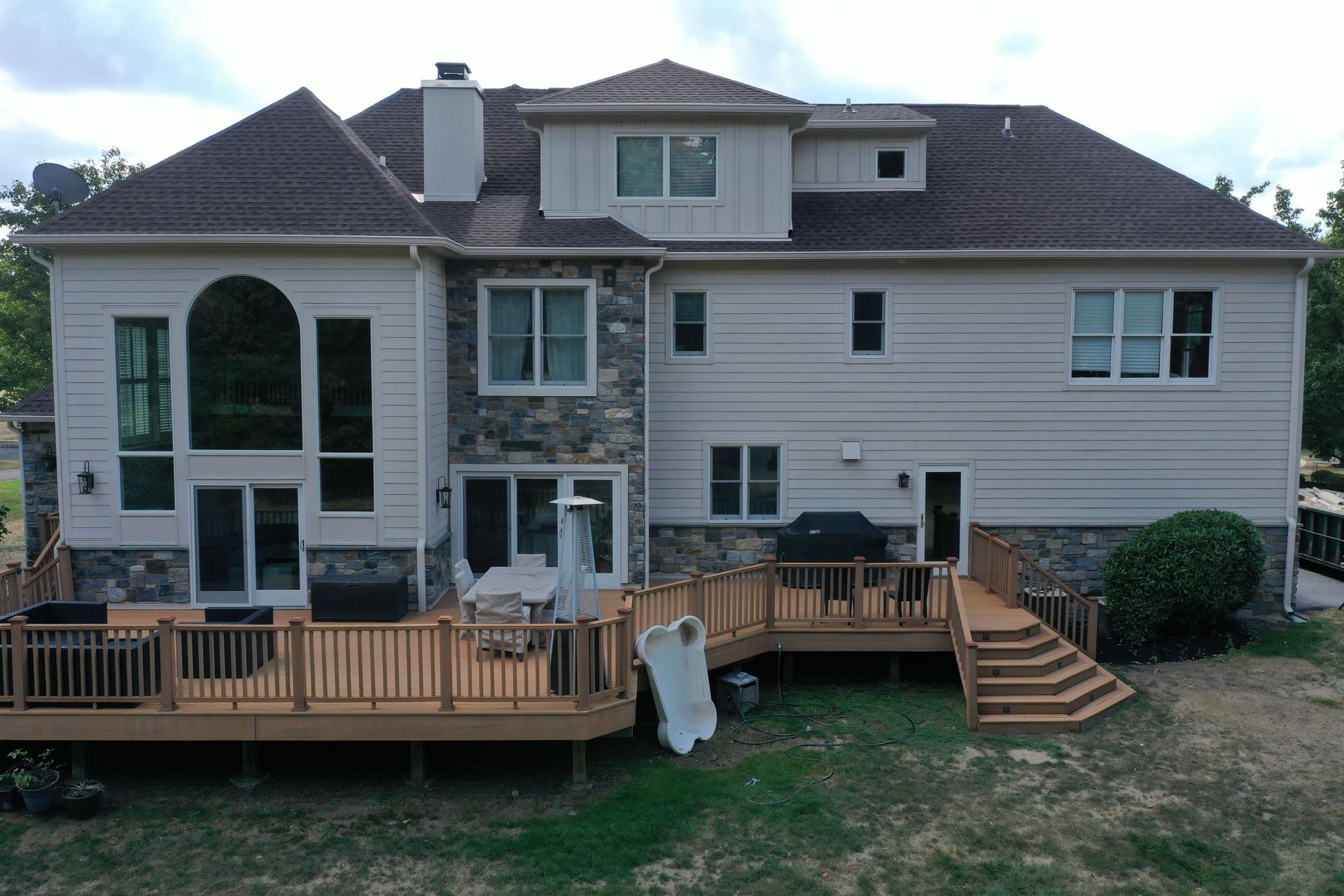 Rear view of a beige two-story house with a brown tile roof and multiple wooden decks.