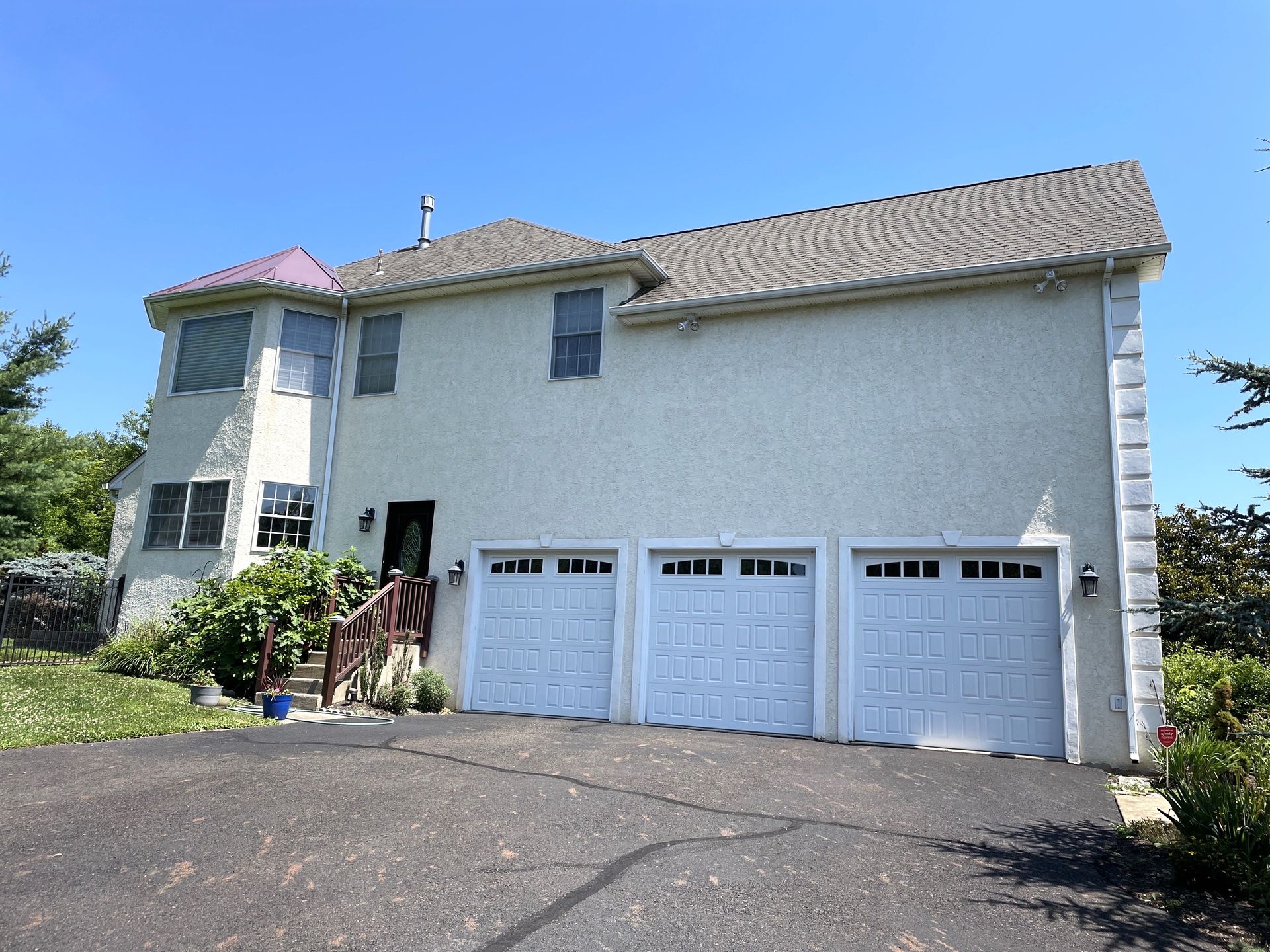 Three-car garage on two-story house with stucco siding, under a blue sky.