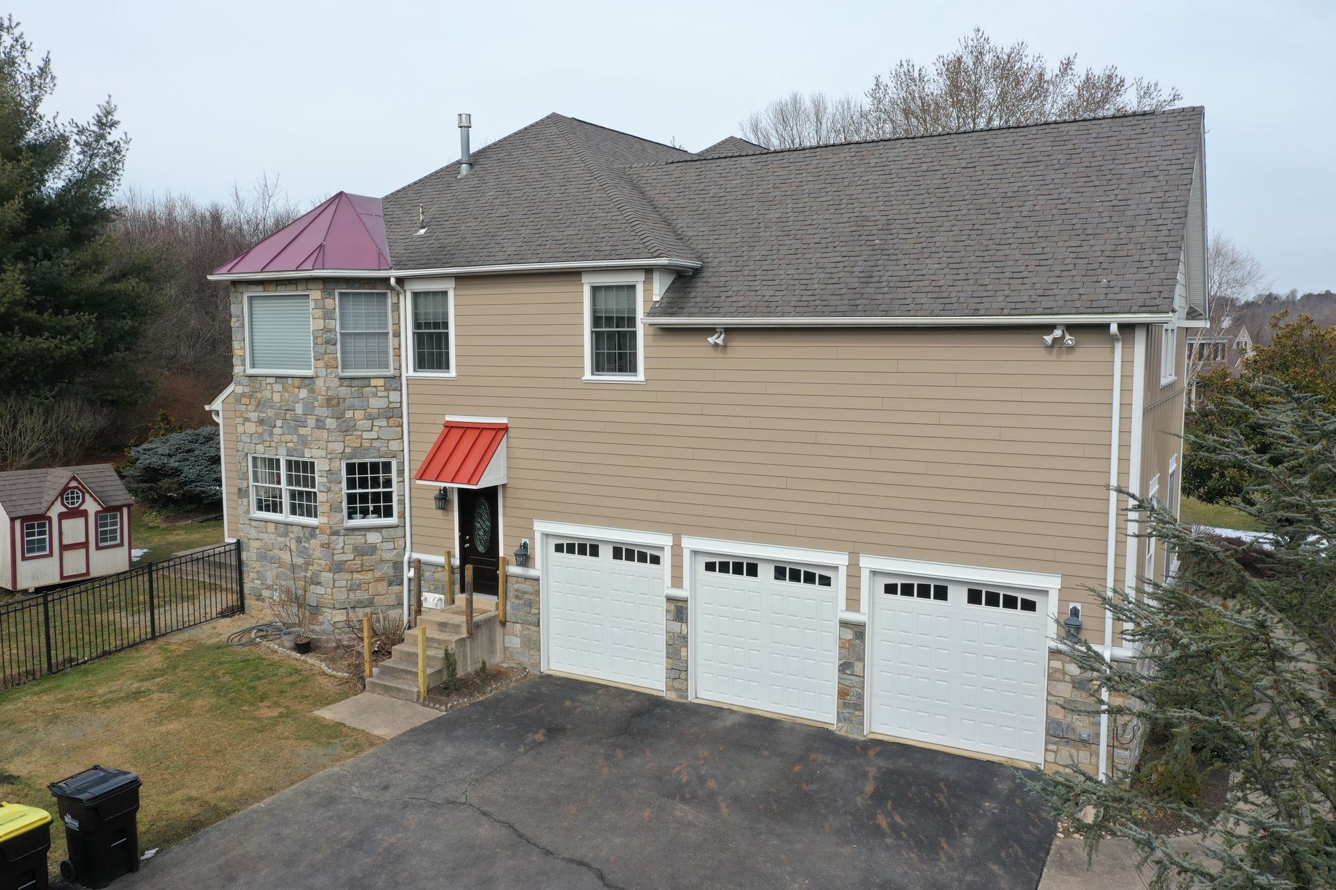 Tan and stone house with three-car garage and red accents; gray asphalt driveway.