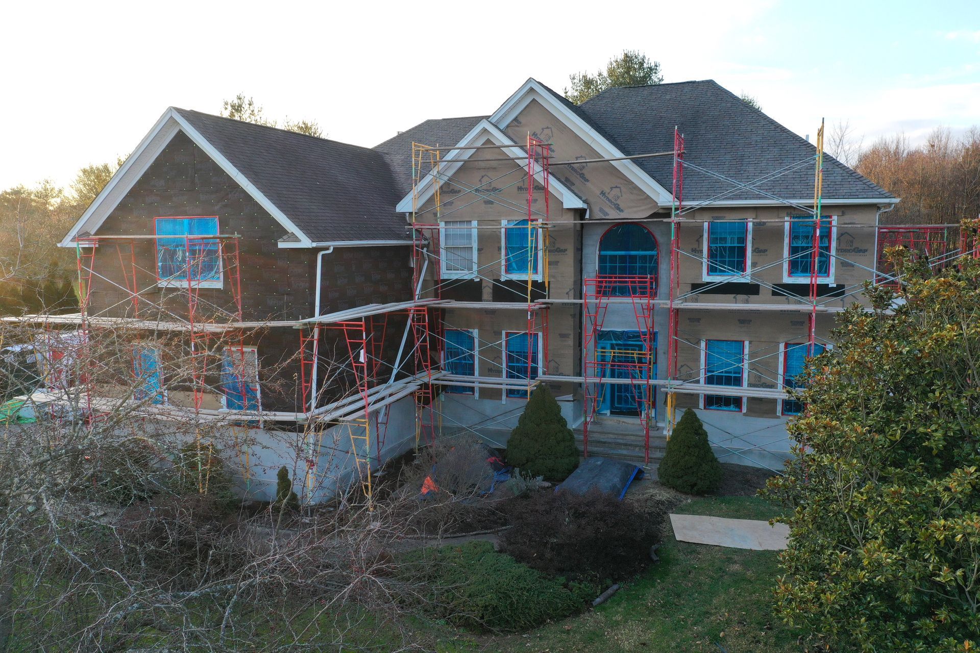 House under construction, red scaffolding, brown roof, blue window coverings, exterior view.