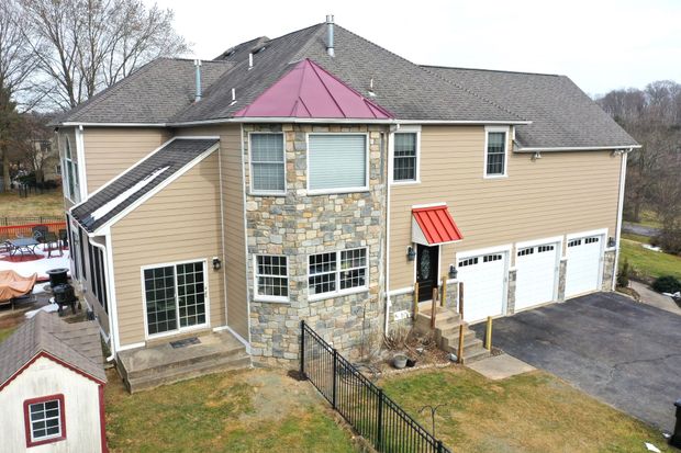 Tan and stone-faced two-story house with a red-roofed turret and garage, viewed from above, with a small shed.