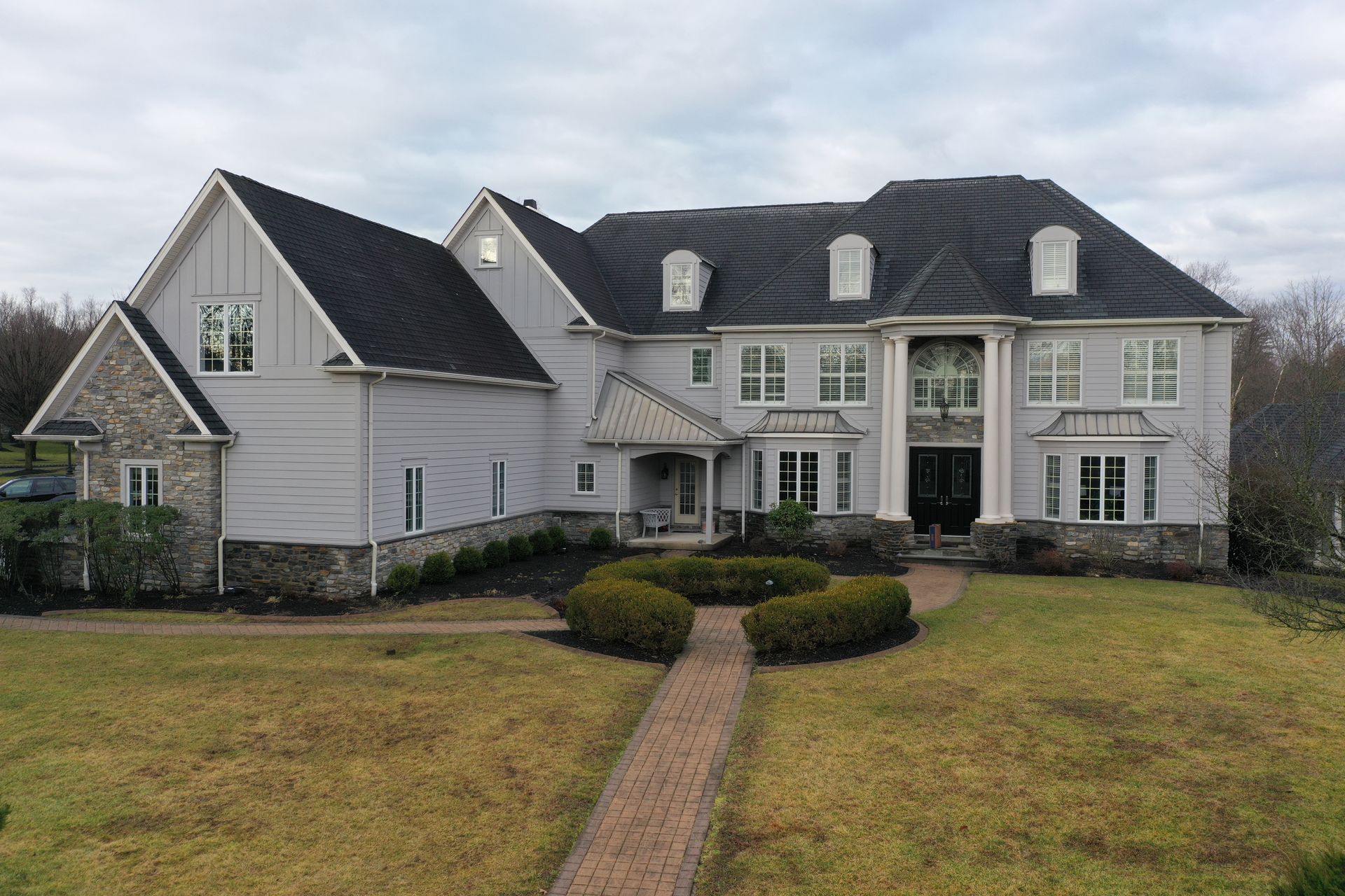 Large gray house with black roof, brick path leading to the entrance, and manicured lawn.