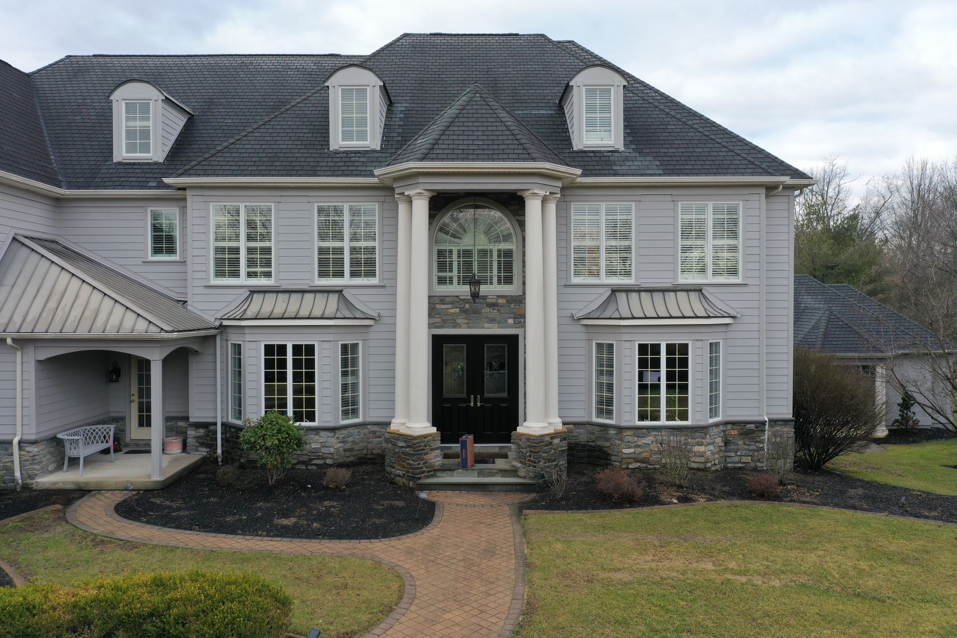 Gray two-story house with stone accents, arched entryway, and dark gray roof; cloudy sky.
