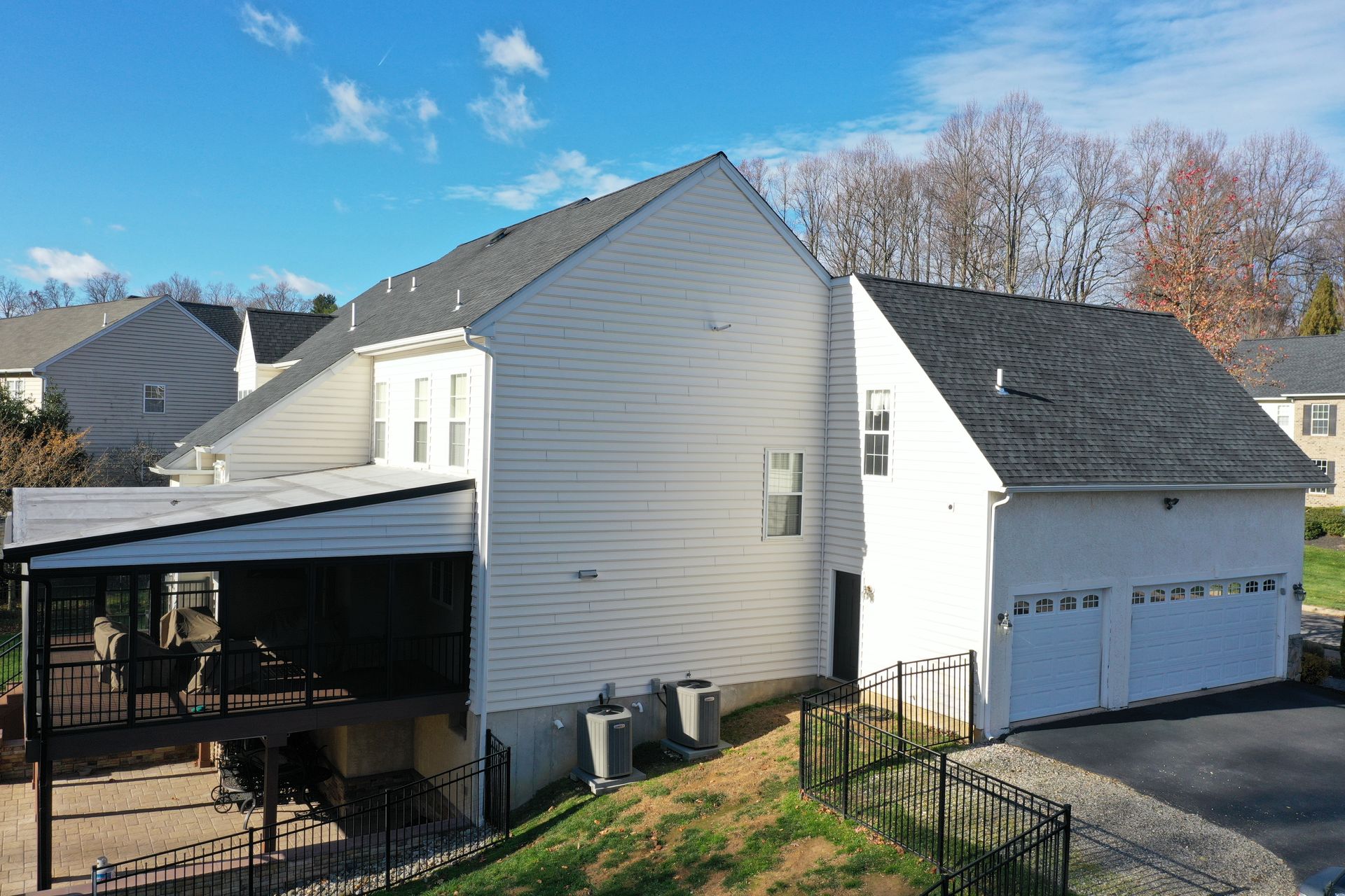 White house with attached garage, covered patio, and black fence.