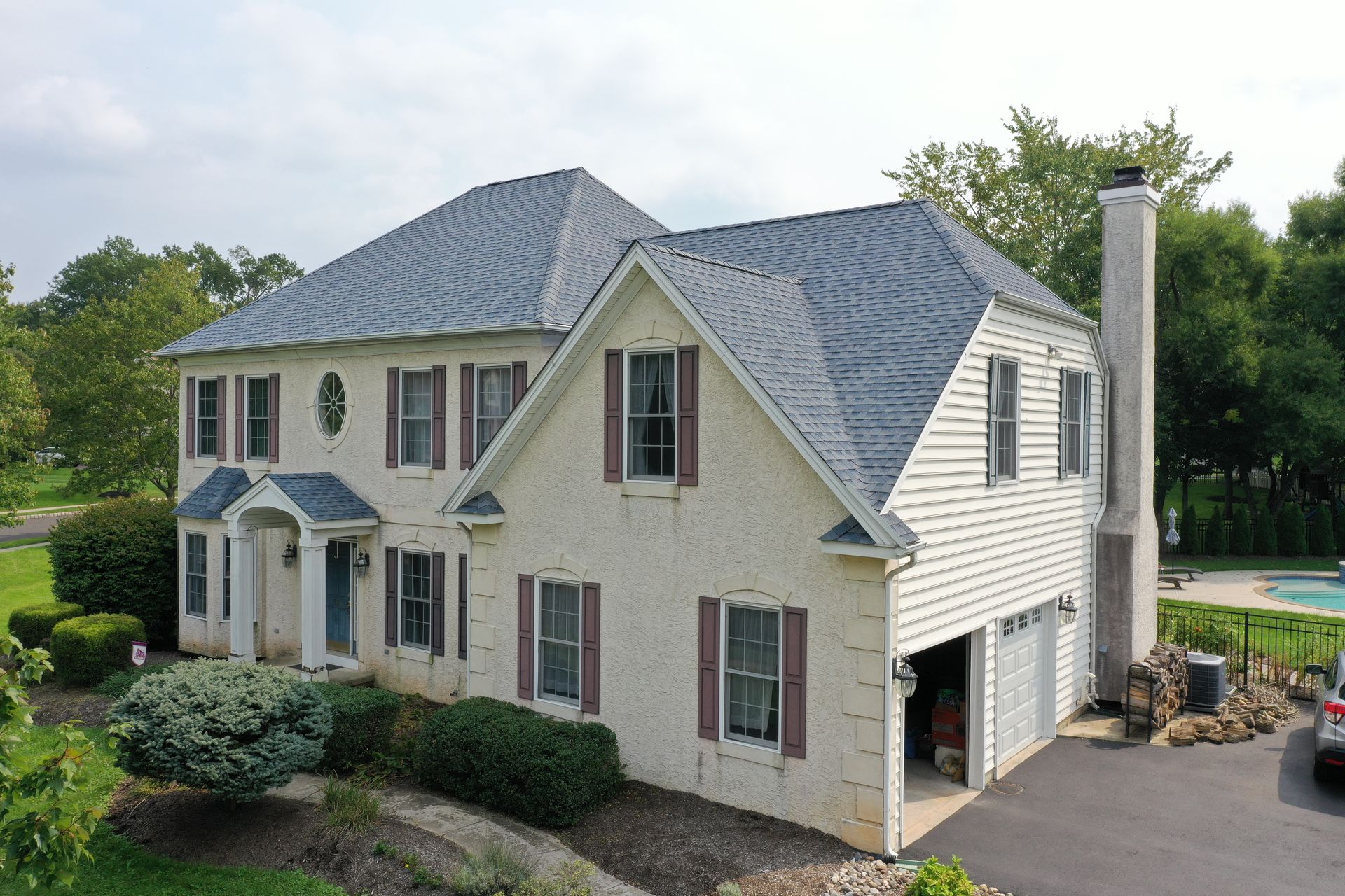 Two-story house with a gray roof and white siding; a driveway and chimney are visible.