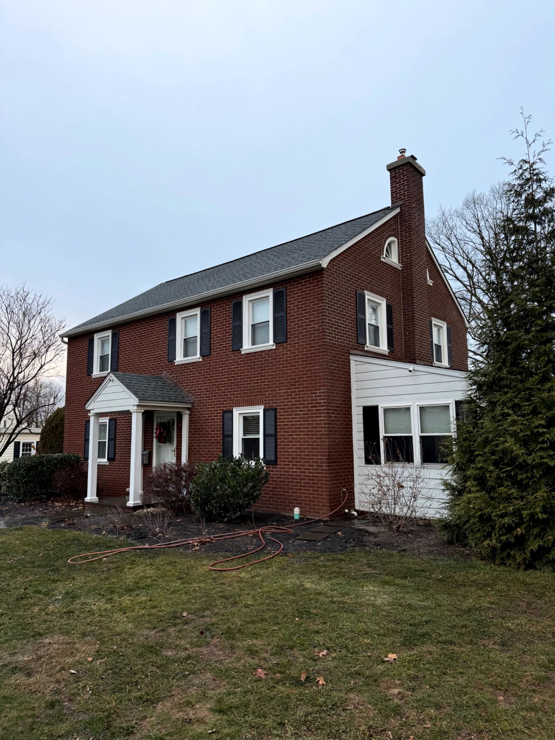 Brick two-story house with black shutters, white trim, and a small porch. Overcast sky, lawn in the foreground.