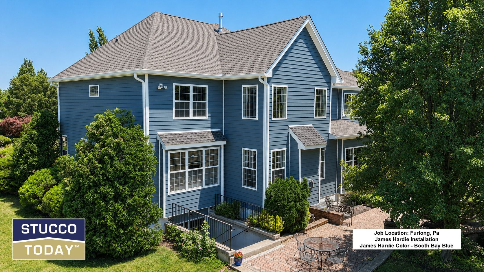 Blue two-story house with white trim and stucco exterior, surrounded by lush greenery and a sunny yard.
