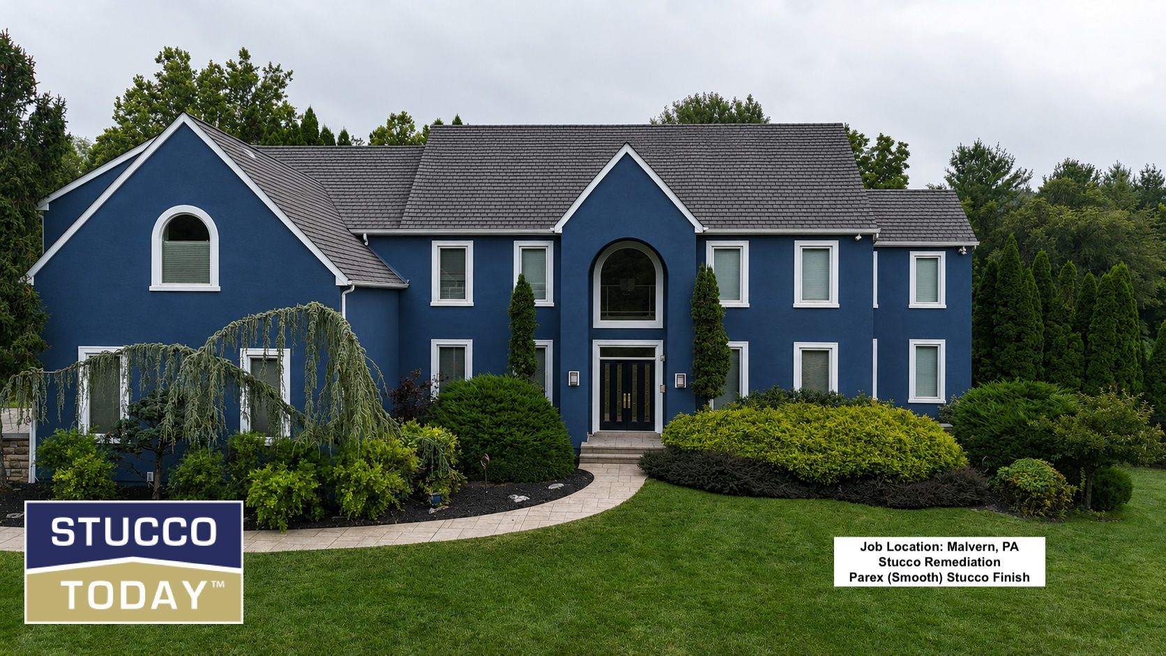 Blue stucco two-story house with white trim, arched entry, and landscaped front yard.