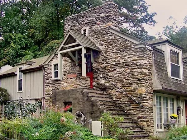 Stone house with chimney, entry stairs, and porch, surrounded by greenery.