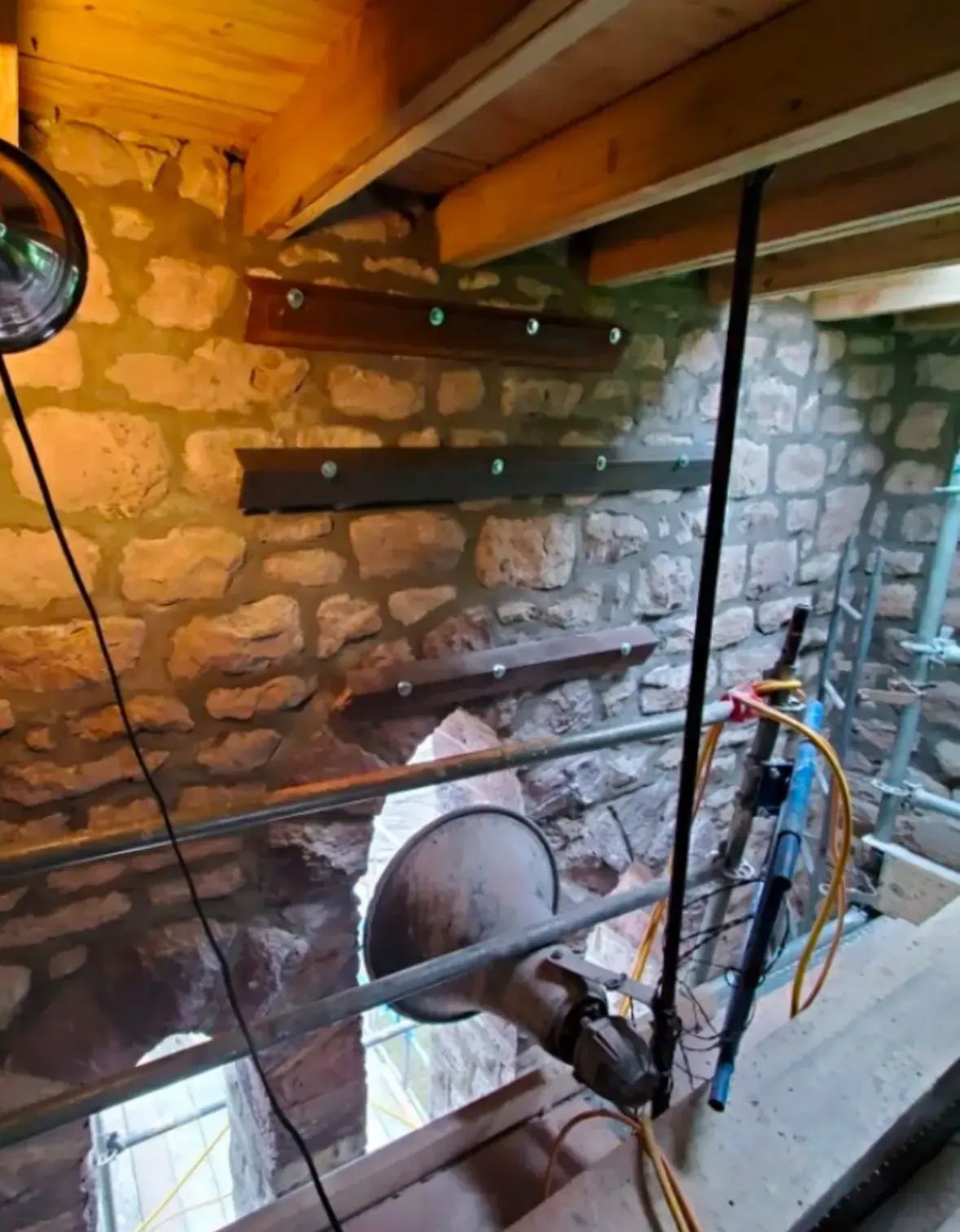 Stone wall with metal beams, support structures. Interior view with light fixture and scaffolding.