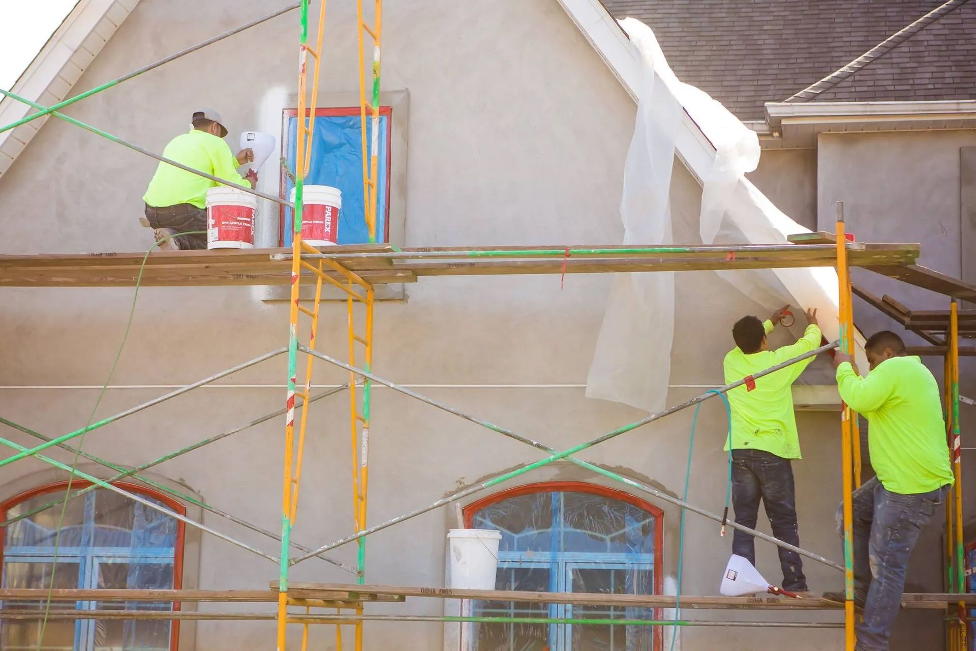 Construction workers in neon vests on scaffolding; applying material to the exterior of a building.