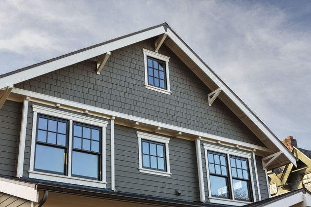 Gray house gable with white trim and multiple windows against a blue sky