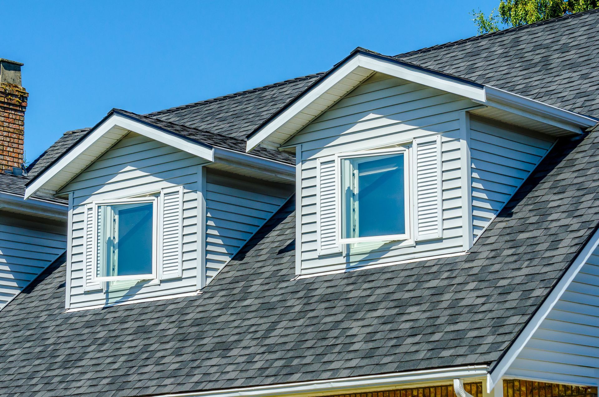 White dormer windows on a gray shingled roof against a blue sky.