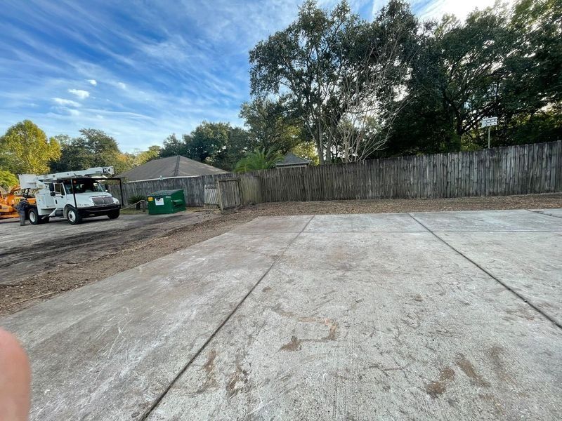 Empty concrete parking lot with a utility truck and wooden fence in the background under a blue sky.