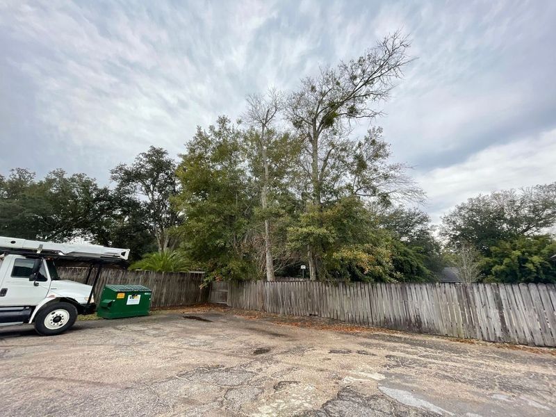A white truck parked near a dumpster and weathered wooden fence with trees in the background under a cloudy sky.