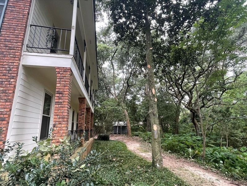 Brick apartment building with a walkway and overgrown trees.