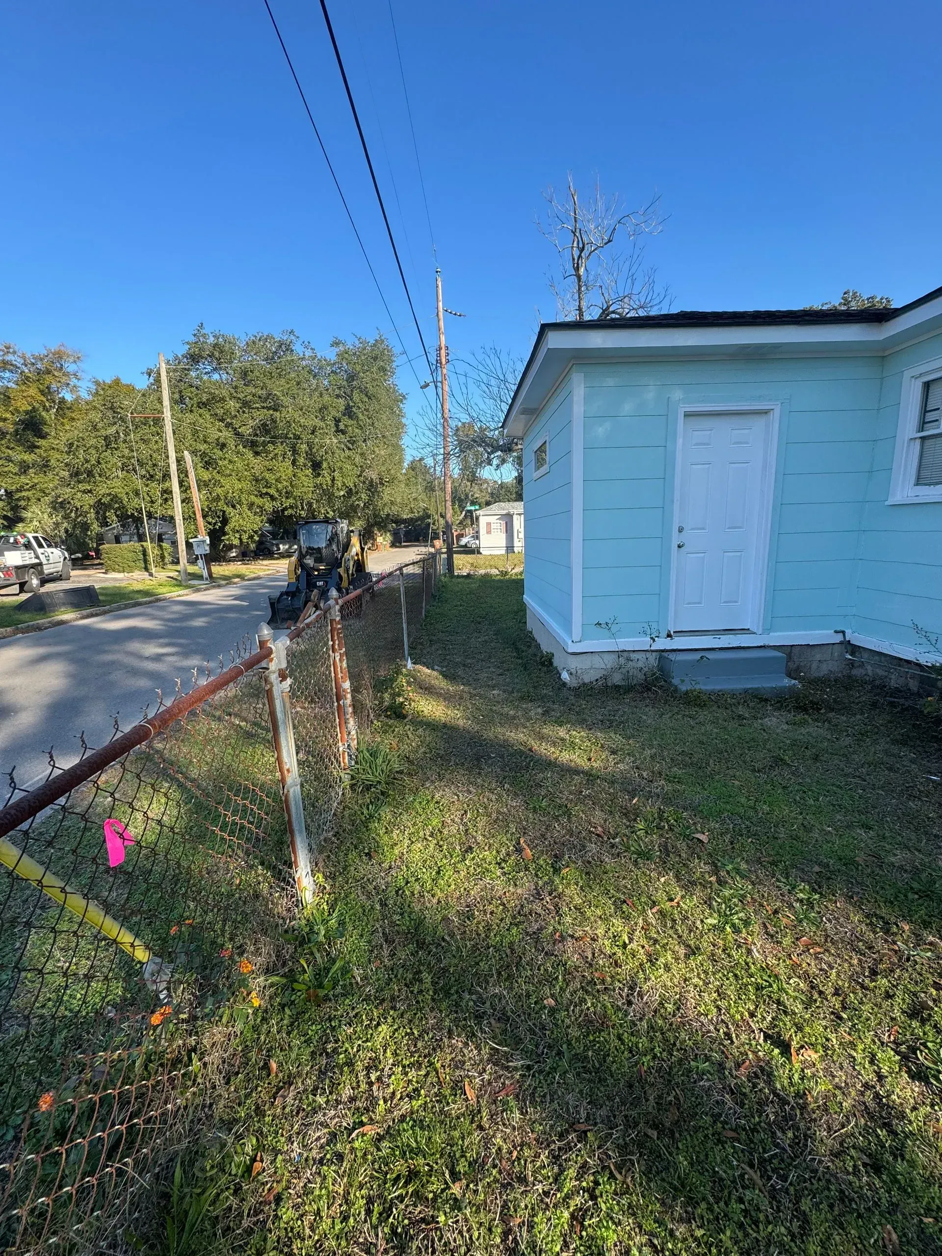 A light blue building with a white door, next to a chain-link fence and a grassy yard.