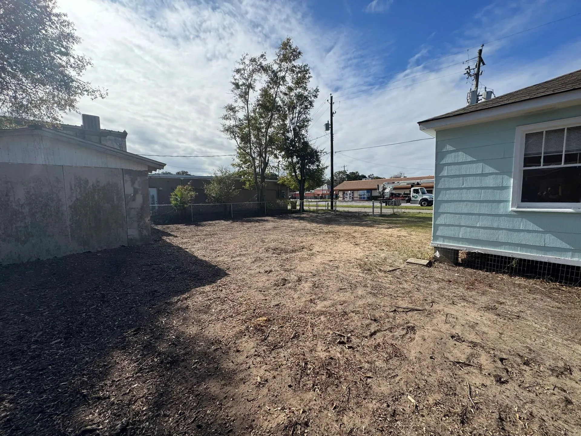 Dirt lot between buildings, with a clear sky and sparse vegetation.
