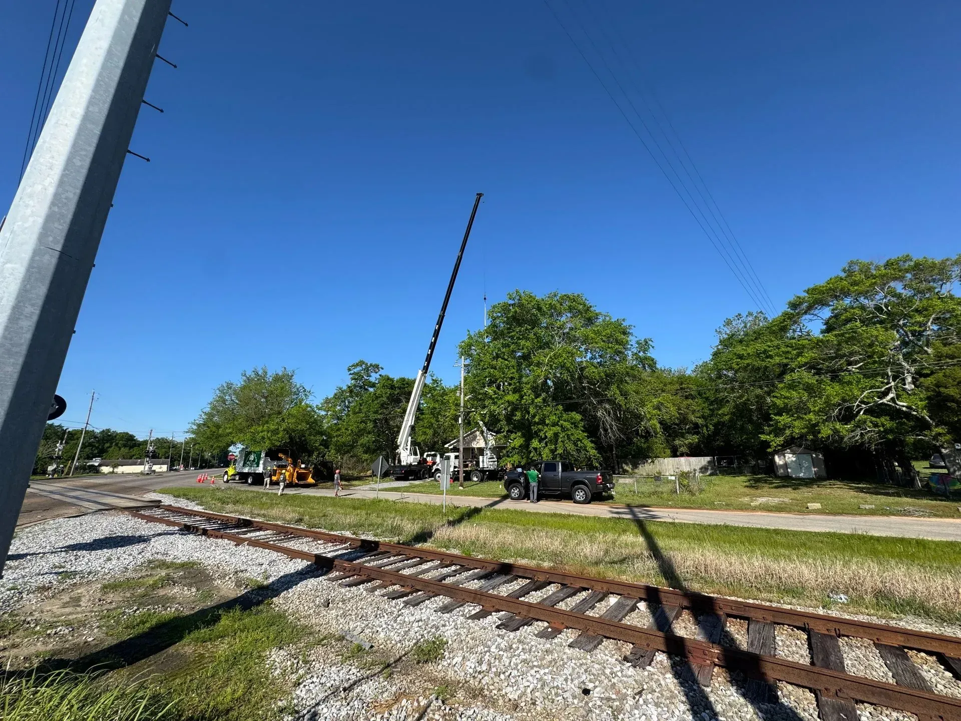 Railroad tracks, utility work in progress with a tall crane, blue sky.