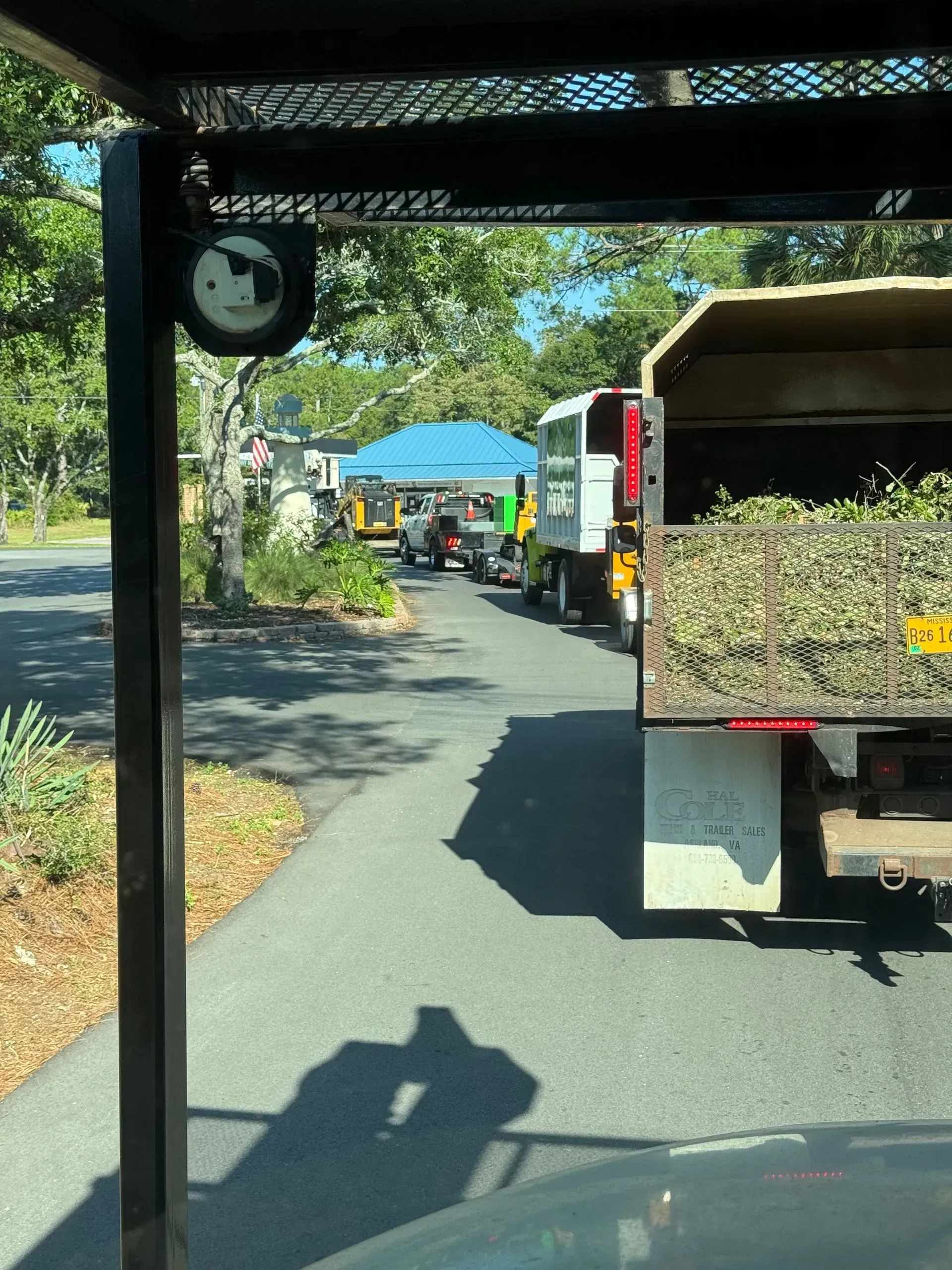 Truck filled with brush in line near a teal tent and other vehicles on a paved road.