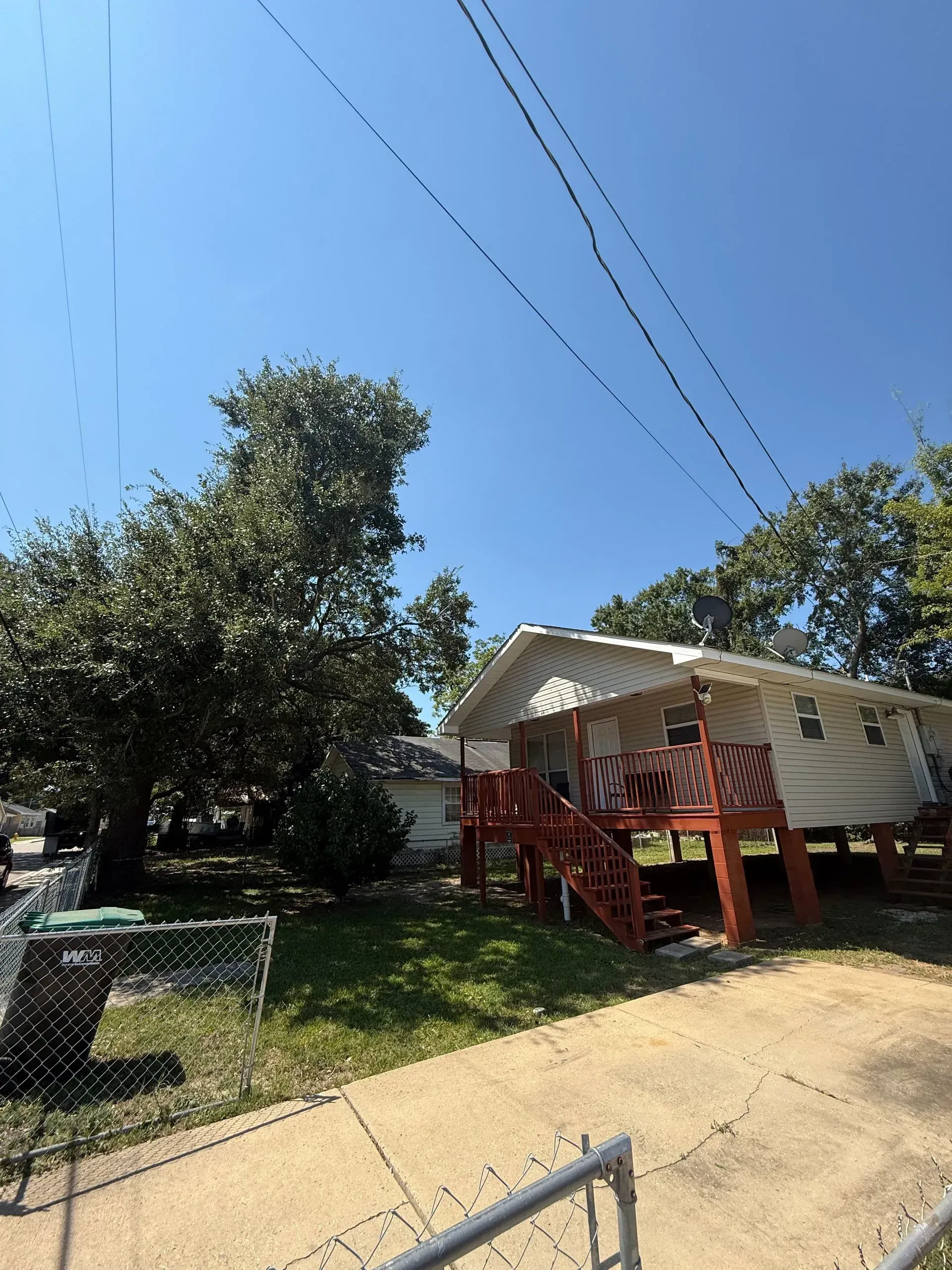 House with raised deck and red stairs, under blue sky, near a large tree and power lines.