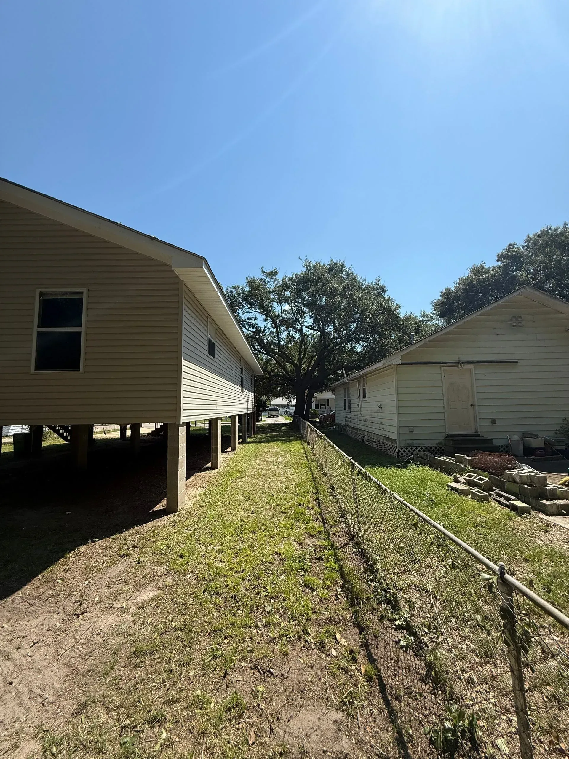 Side view of two buildings with a chain link fence and a grassy yard under a blue sky.