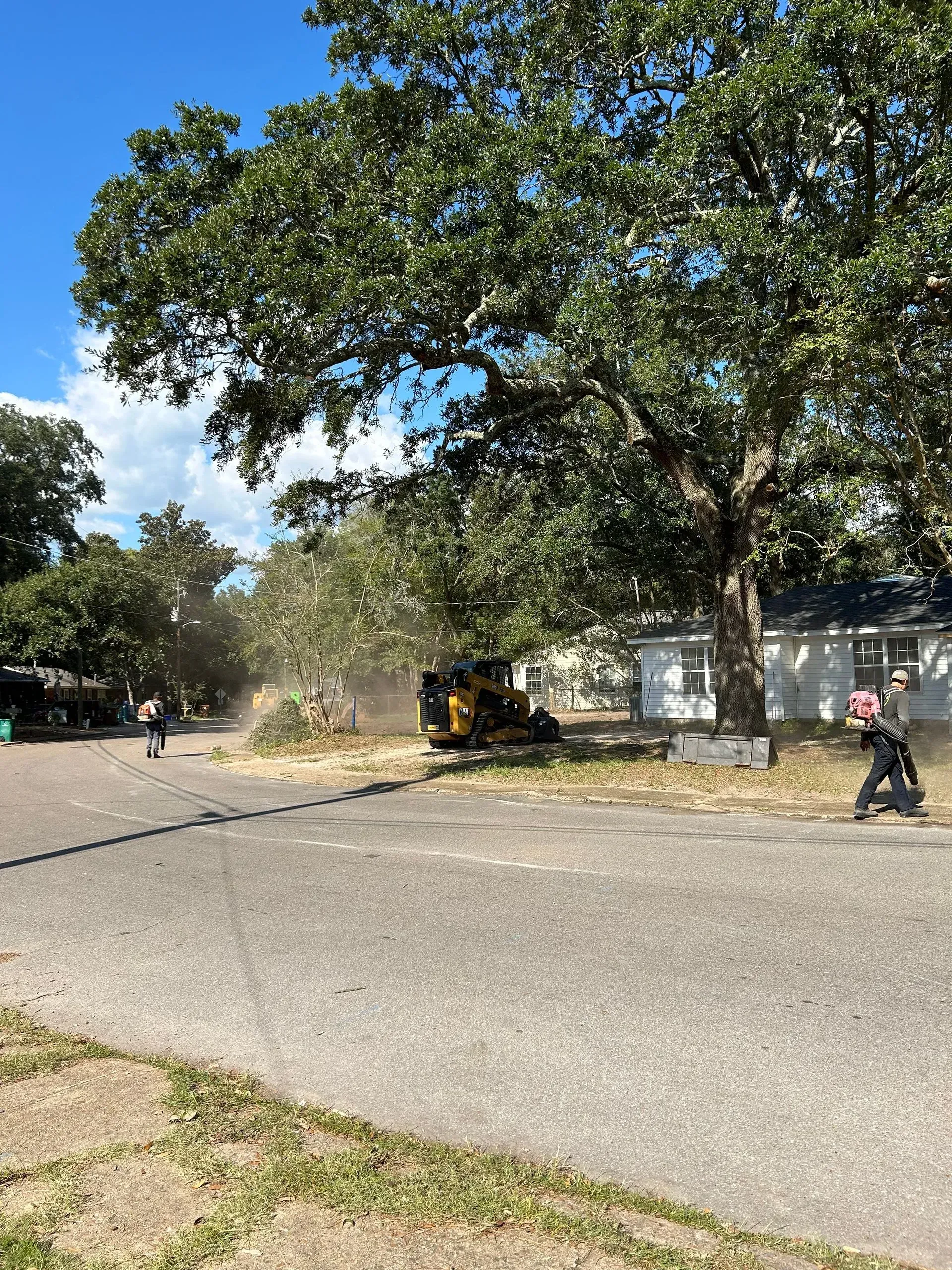 Construction site with tree branches being shredded; people, machinery, and a house.