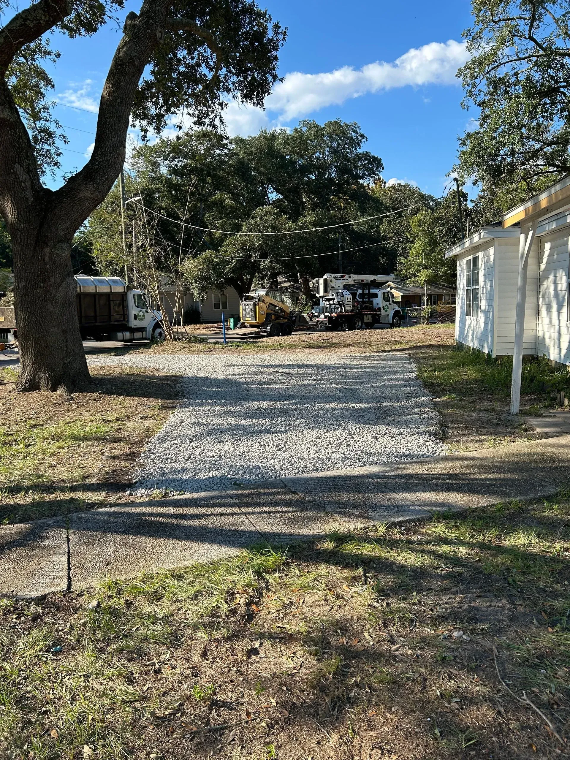 Gravel driveway leading to parked RVs and small white building under a blue sky, trees on either side.
