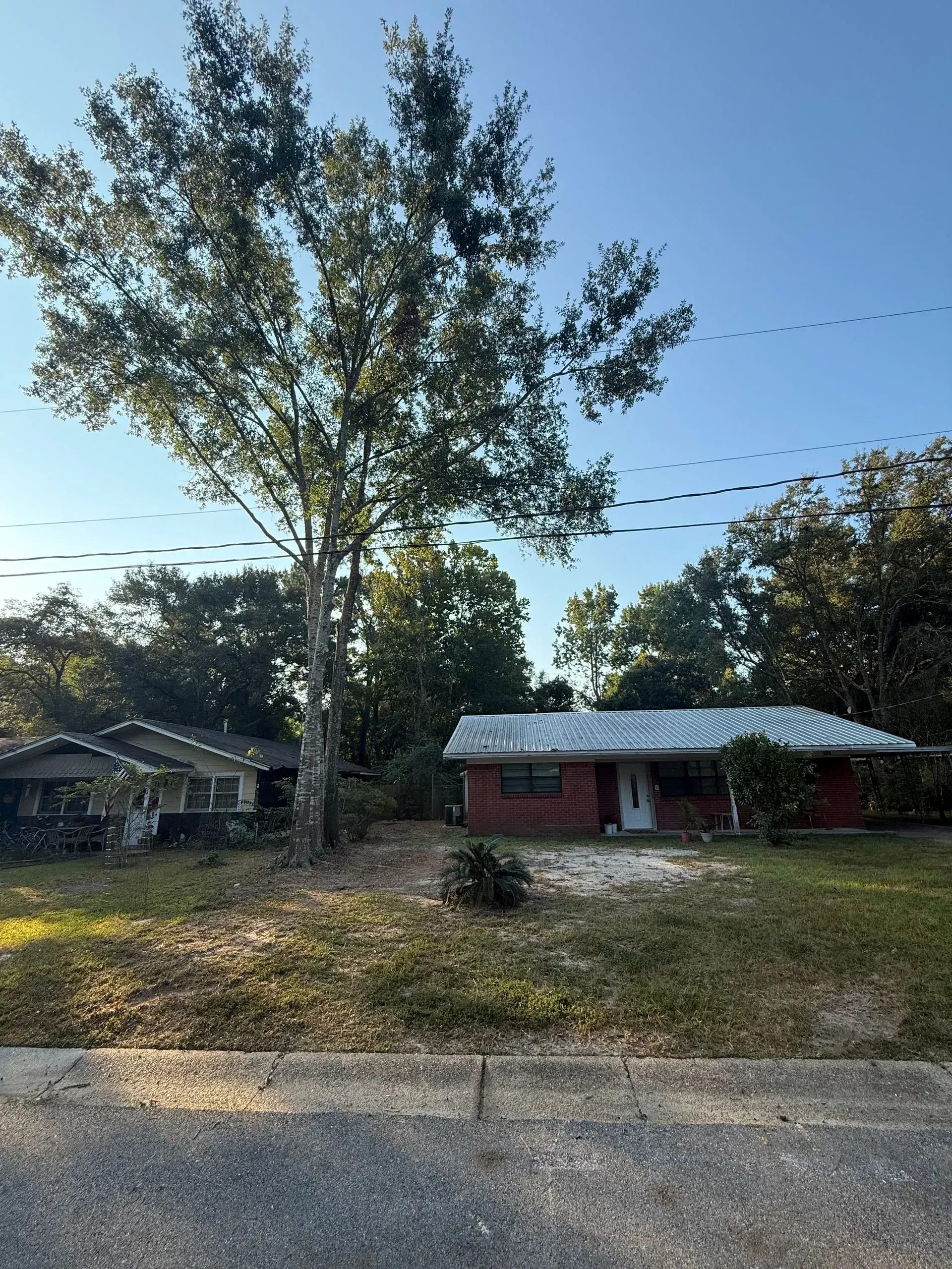 Two houses with trees against a blue sky; one is red and the other grey.