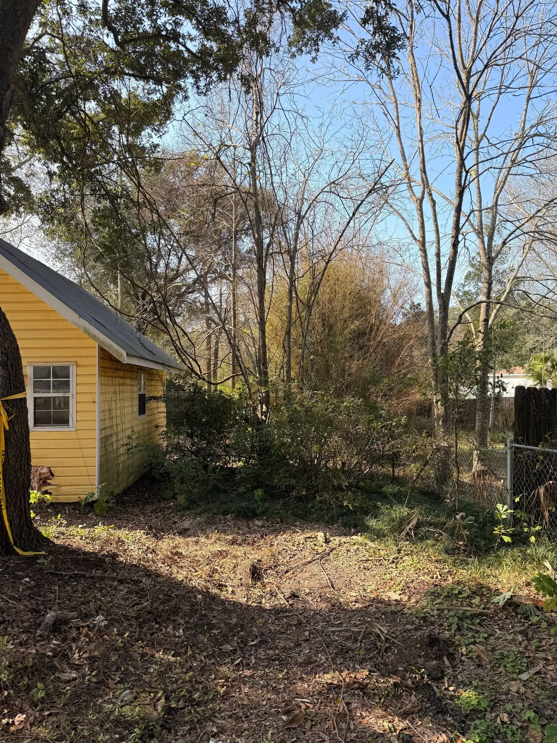 Yellow building next to a wooded area with trees and ground covered in leaves.