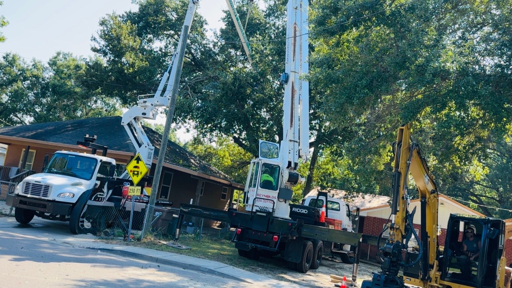 Utility trucks and an excavator working on power lines near a house.
