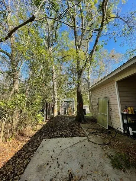 Backyard with a concrete patio, trees, and a beige building under a blue sky.