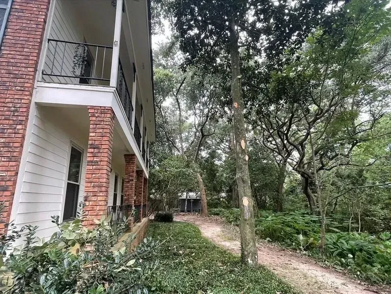 Apartment building next to a dirt path leading into a wooded area.