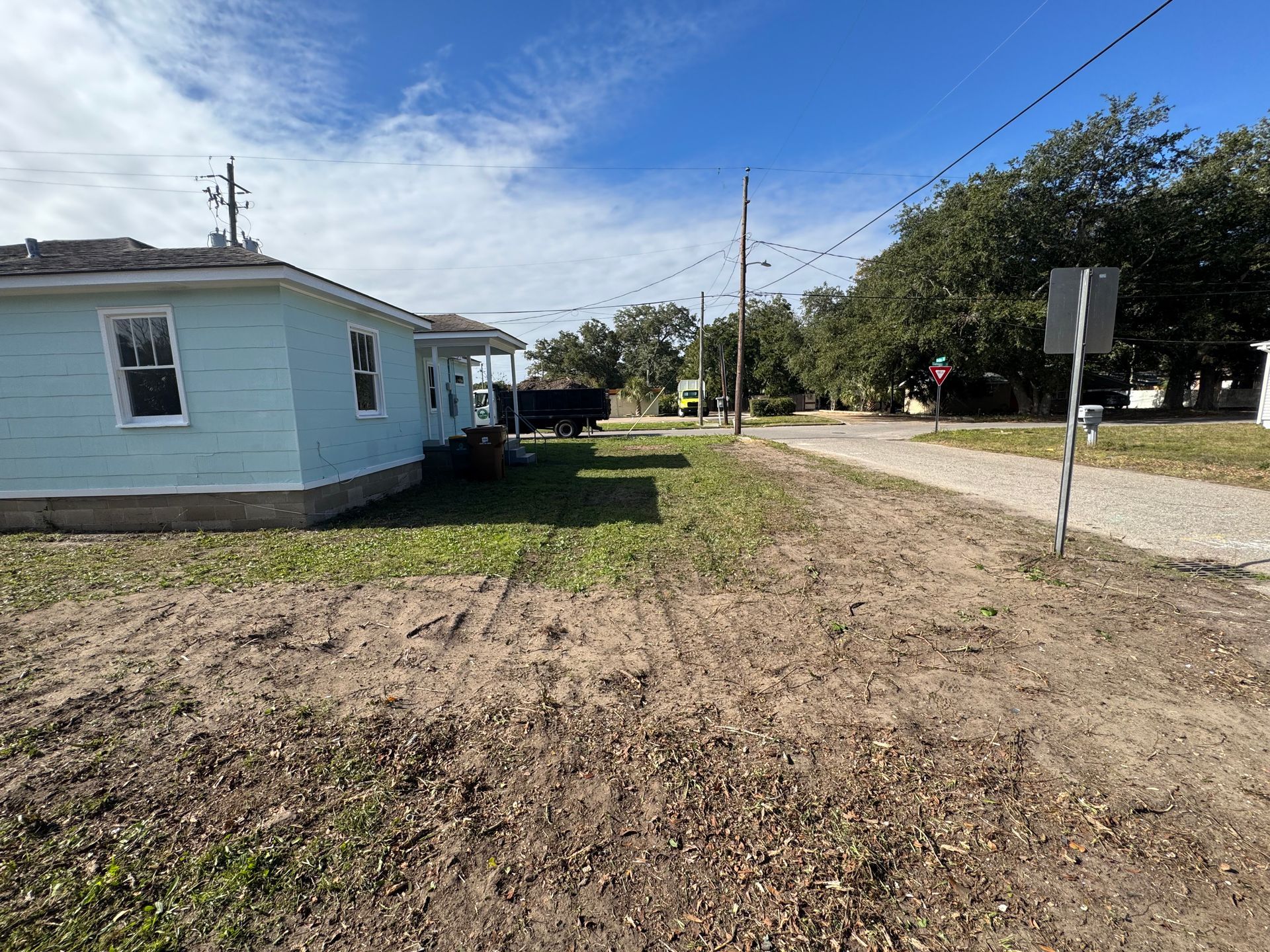 A light blue house sits next to a dirt path and a gravel road under a blue sky.