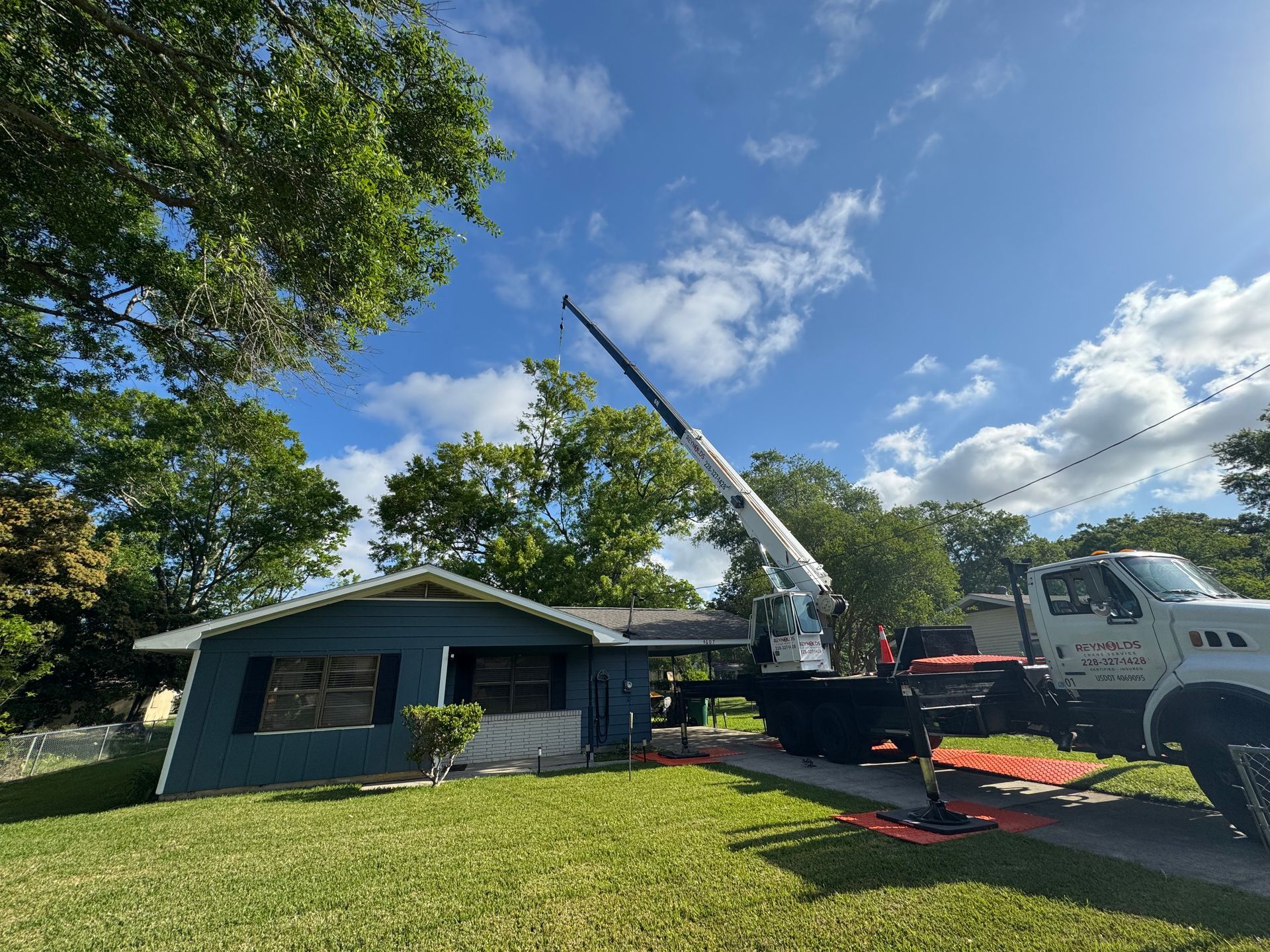 A crane truck working near a blue house on a sunny day.