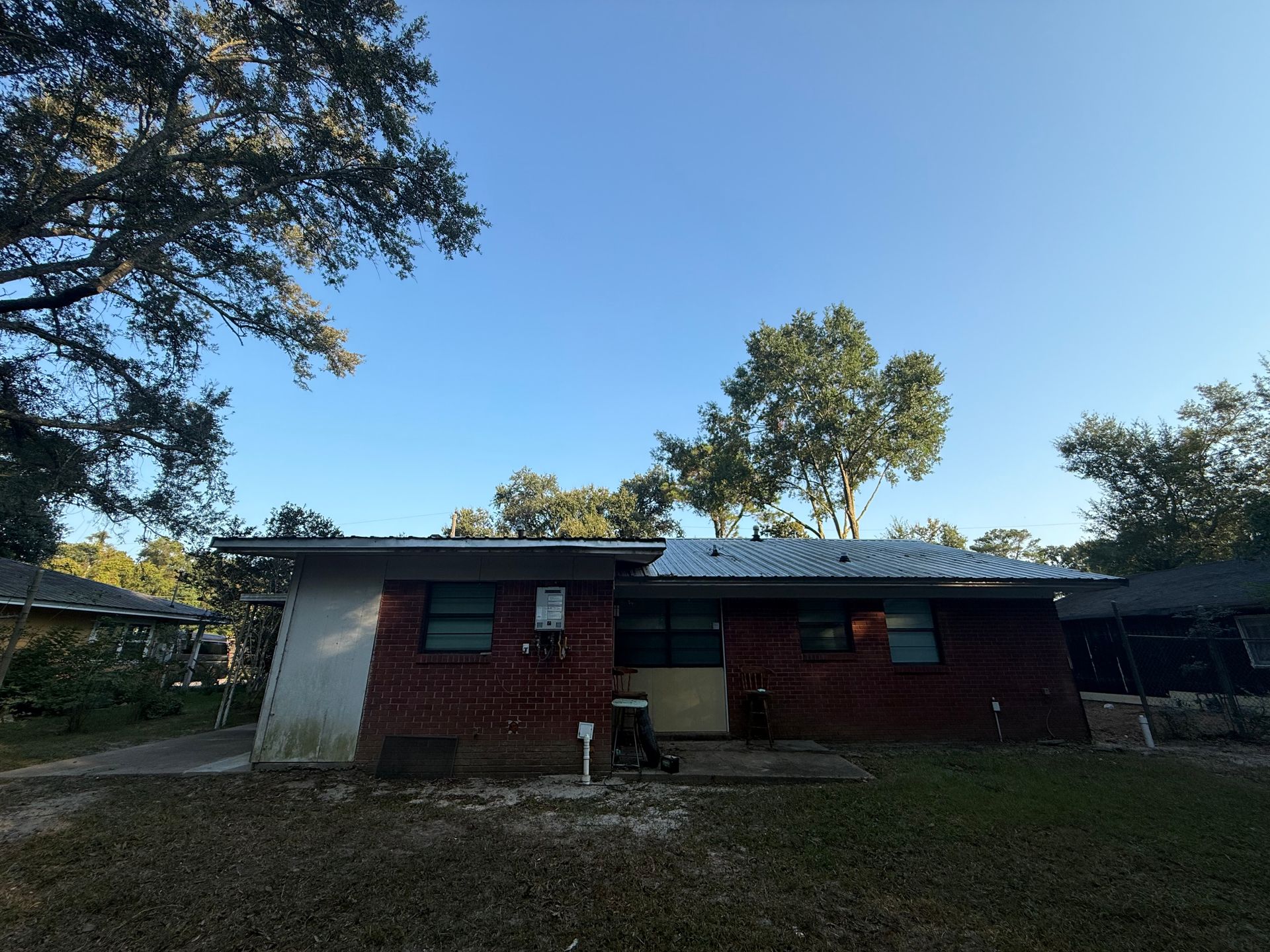 A single-story brick building with a metal roof under a blue sky, surrounded by trees.