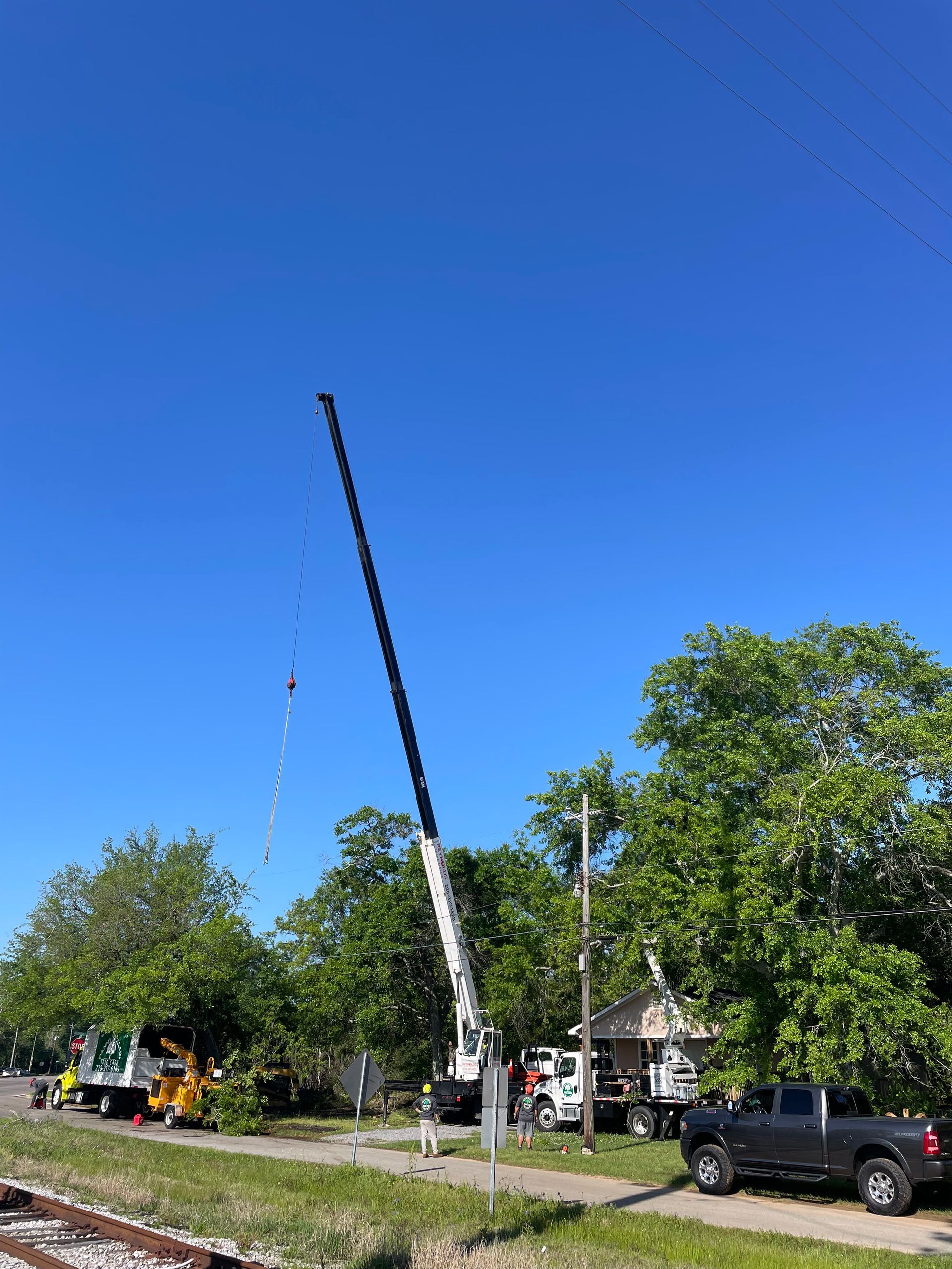 A crane working on power lines; other utility trucks and a black pickup truck are in the scene. Blue sky, green trees.