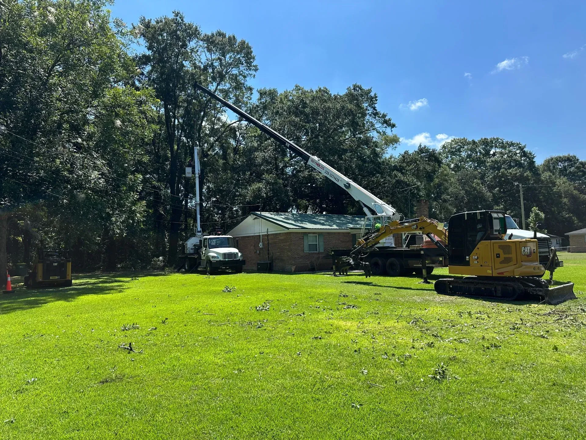 Crane removing roof from a house on a sunny day. Heavy machinery and workers are present in grassy yard.