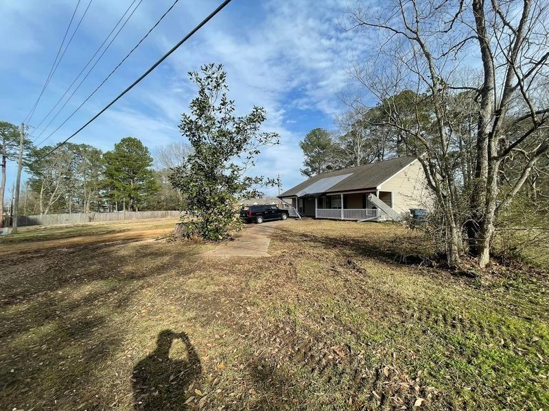 A single-story beige house with a porch. A person's shadow is visible in the foreground. Overcast sky.