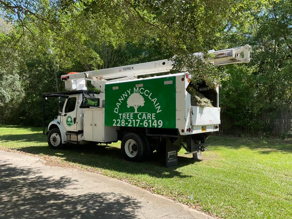 White Danny McClain Tree Care truck parked on grass; green tree and shrubbery in background.