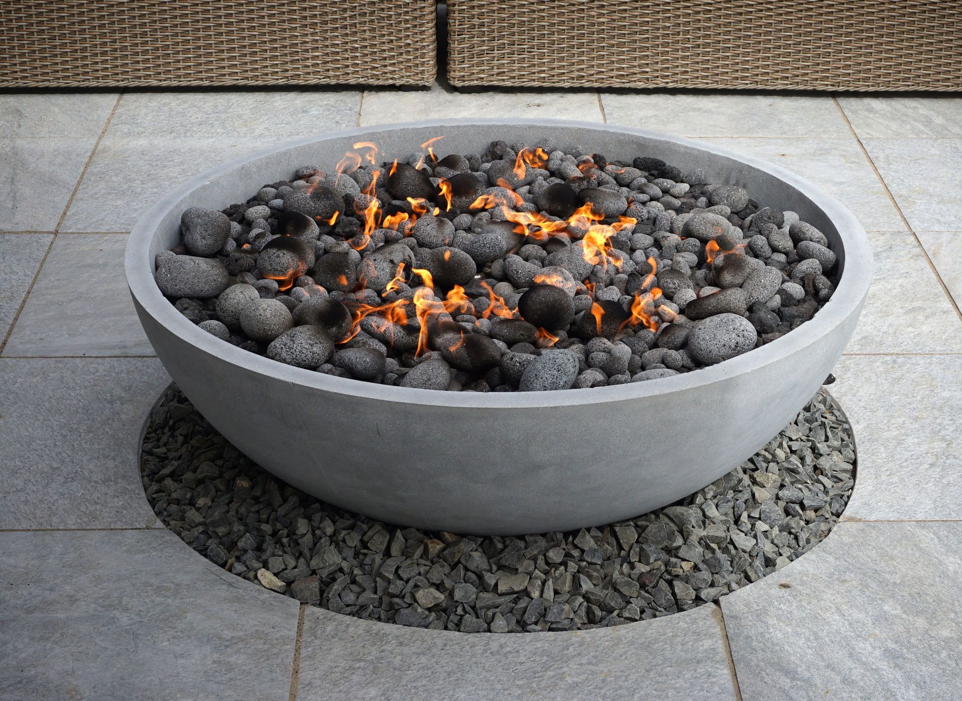 Fire pit in a gray stone bowl, with burning flames and dark stones, set on a stone patio.