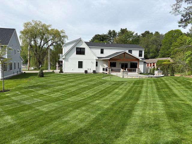 White farmhouse with covered porch beside a neatly striped green lawn and trees under a cloudy sky