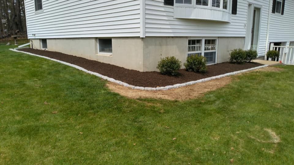 Mulched flower bed with shrubs along the corner of a white house on a grassy lawn