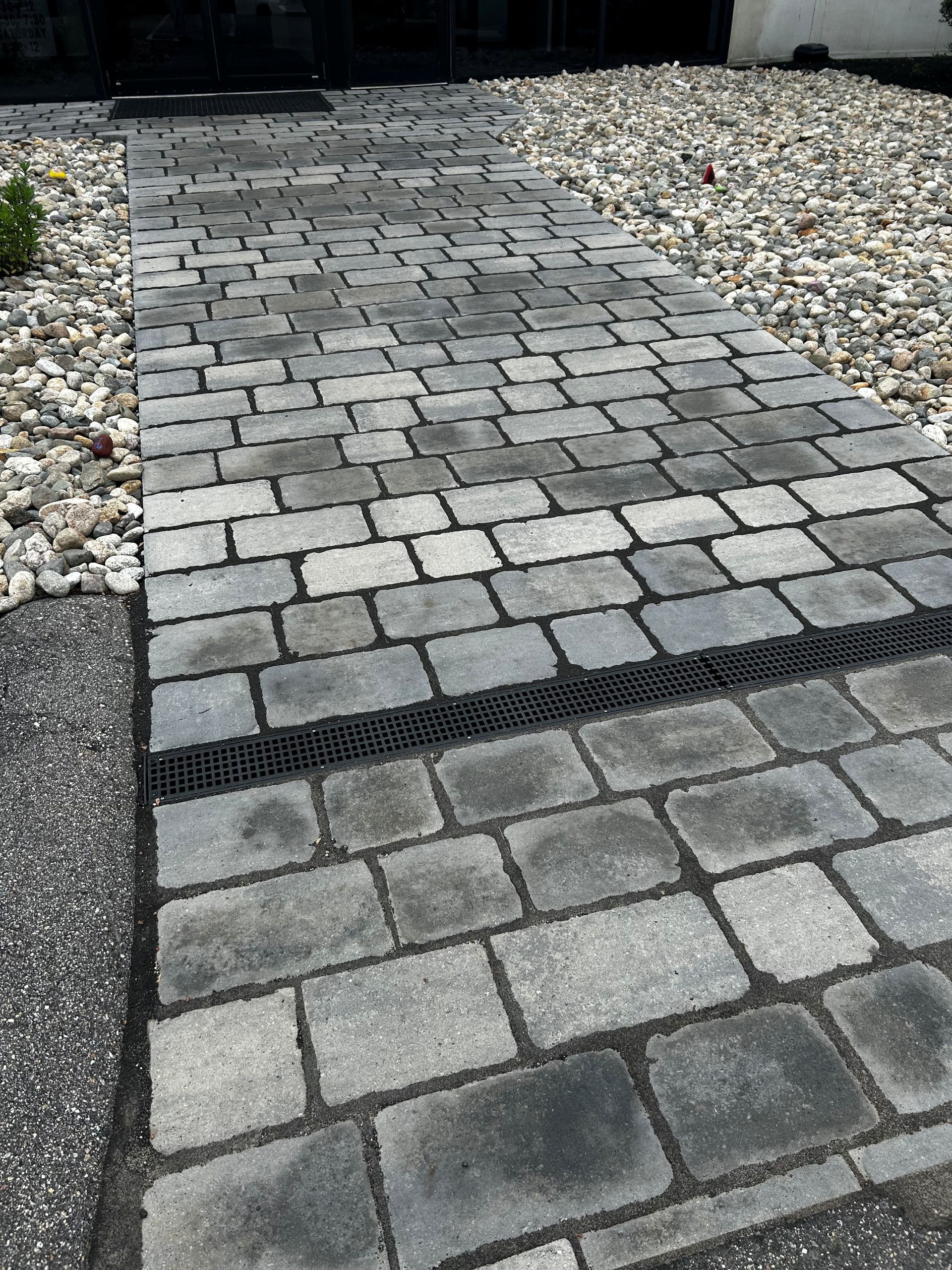 Gray stone paver walkway bordered by white gravel, with a darker strip across the path