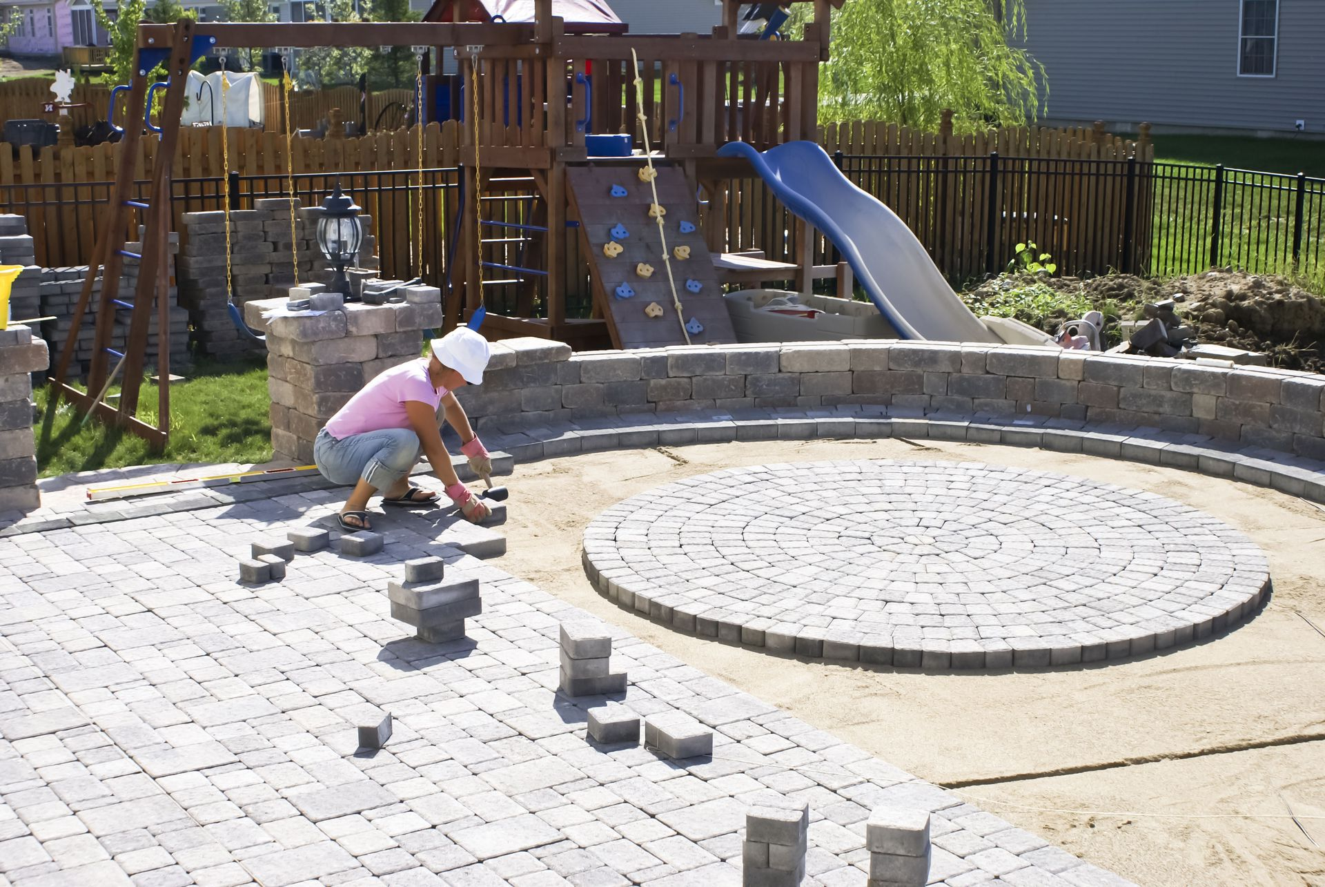 Woman laying paving stones in backyard with playground.