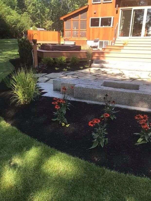 Landscaped backyard with mulch beds, flowers, and a patio leading to a house.